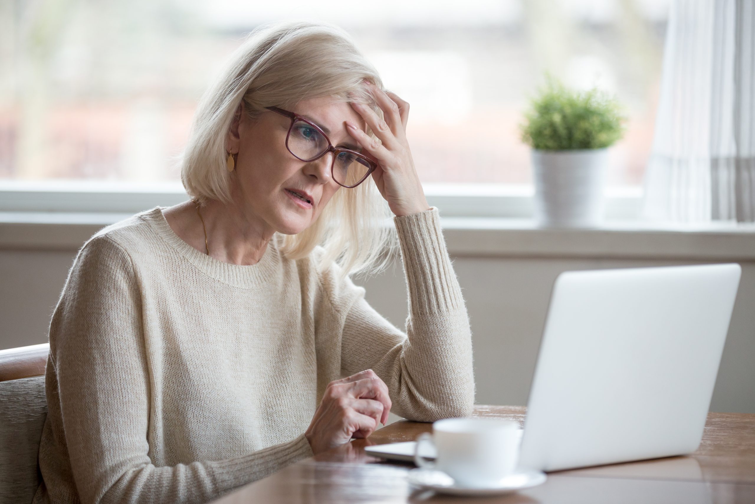 Confused mature woman thinking about online problem looking at laptop